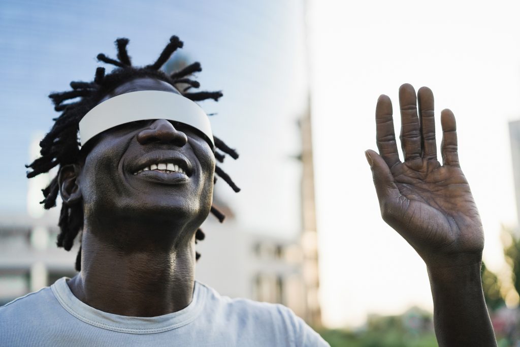 African man having fun using augmented reality glasses outdoor 
